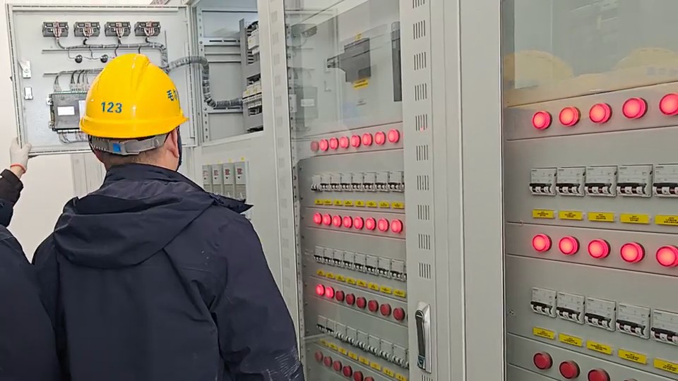 Personnel visually inspect controls and connections in an open electrical cabinet.